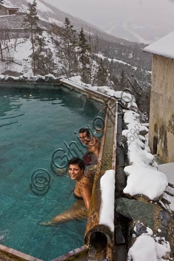 A couple of guests relaxing in the open-air thermal pool at Bagni Vecchi in Bormio, with Alpine mountain backdrop