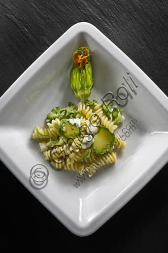 A dish of rotini pasta with zucchini and melted mozzarella cheese, garnished with basil.