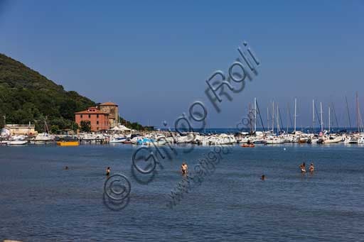 Panoramic summer view of the Baratti Gulf in Tuscany, Italy, with the small tourist port and the beach crowded with bathers.