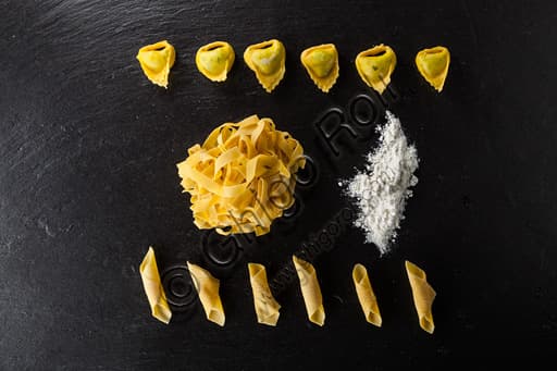 Raw composition of artisanal fresh egg pasta: tagliatelle, stuffed tortelloni, and garganelli with flour