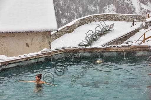 Panoramic view of the open-air thermal pool at Bagni Vecchi in Bormio, with guests relaxing in the warm waters against a mountain backdrop