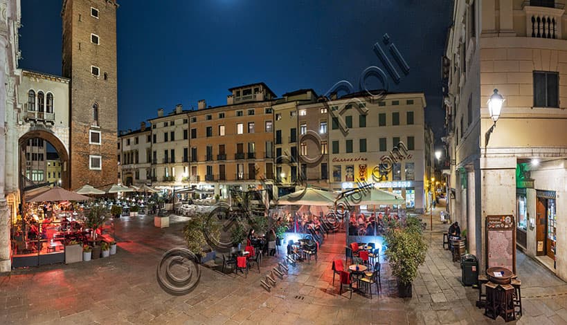 Veduta notturna di Piazza delle Erbe a Vicenza con la Torre medievale del Girone sullo sfondo e i tavolini di bar e ristoranti