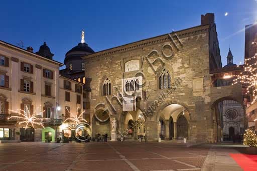Night view of the illuminated Palazzo della Ragione in Piazza Vecchia, Bergamo Alta. On the left, the historic facade of the Caffé del Tasso.