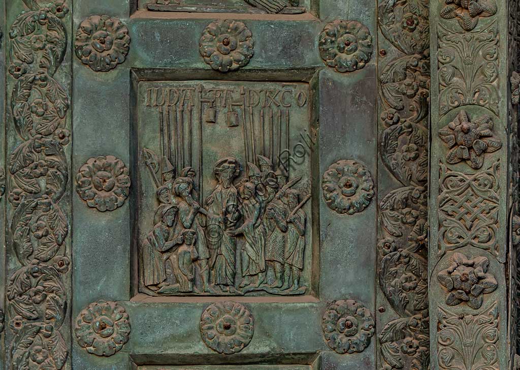 Duomo di Monreale, Porta di Bonanno Pisano (1185-6): formella bronzea con "Il Bacio di Giuda" (scena dal Nuovo Testamento).La porta è firmata: "Bonanno civis pisanus". Iconograficamente nei cinque ordini inferiori vi sono scene del Vecchio Testamento, sette dedicate alla storia di Adamo ed Eva, e altre sei ad altrettante coppie di profeti mentre nei cinque superiori scene del Nuovo, al sommo Cristo e Maria nella gloria del Paradiso.