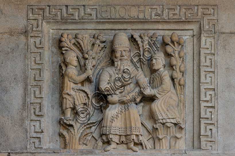 Fidenza, Duomo (Cattedrale di S. Donnino), facciata: bassorilievo con "Il profeta Enoch” di Benedetto Antelami e bottega.Il personaggio è assiso su un faldistorio nel mezzo d’un giardino (Il Paradiso) rappresentato da due alberi carichi di frutti. È vestito con una tunica e un soprabito più corto con orli lavorati, e porta in testa un cappello troncoconico. Benedice con la destra, e nella sinistra tiene un oggetto che sembra un frutto. Ha ai fianchi due assistenti; quello a destra gli porge un contenitore cilindrico, mentre quello a sinistra è arrampicato su un albero intento a cogliere dei frutti. 