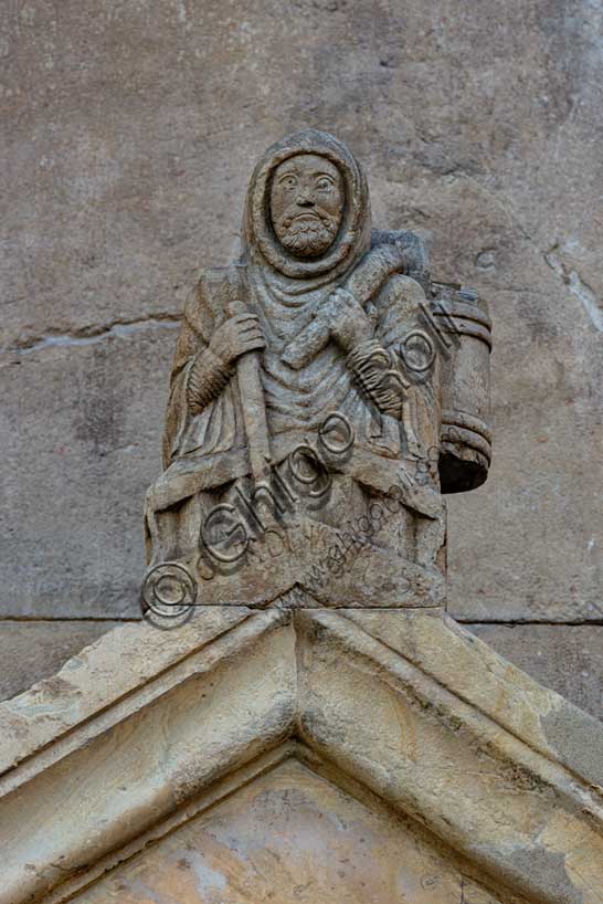 Fidenza, Duomo (Cattedrale di San Donnino), acroterio del portale destro: “Raimondinus vilis”, il Povero Raimondino. In questa figura viene tradizionalmente riconosciuto  San Raimondino Zanfogni, detto Palmerio, di Piacenza (1140 – 27 luglio 1200), un laico che sarebbe stato pellegrino in Terrasanta (da qui il soprannome) e poi a San Giacomo di Campo Stella. Tornato a Piacenza avrebbe assistito e difeso i poveri della sua città e avrebbe fondato un ospedale. 