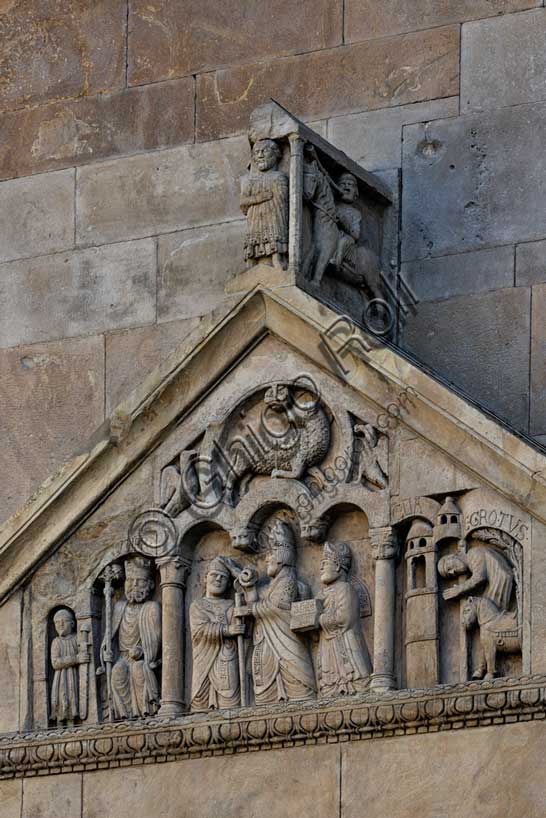 Fidenza, duomo (Cattedrale di San Donnino), portale sinistro, timpano. Nel frontone si leggono, da sinistra, tre scene: L'imperatore Carlo Magno, con un armigero alla sua destra;Papa Adriano II che porge all'arciprete di San Donnino la mitria e il pastorale (simboli della dignità episcopale); il miracolo dell'ammalato guarito (miracolo compiuto da San Donnino).Nell’acroterio sul timpano, é raffigurato un personaggio, probabilmente Oberto II Pallavicino condottiero posto da Federico II di Svevia alla guida della città dal 1249 al 1268.Opera di Benedetto Antelami e bottega.