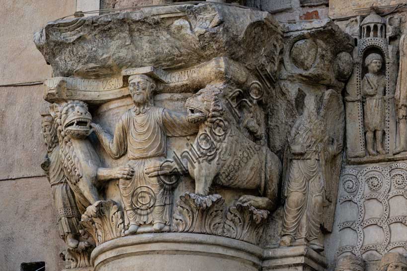 Fidenza, duomo (Cattedrale di San Donnino), sculture tra il portale maggiore e quello di sinistra. Particolare del semicapitello con “Daniele nella fossa dei leoni”. Il semicapitello figurato che raffigura nella parte frontale la scena biblica – di simbologia cristologica – del profeta Daniele che gettato nella fossa è attorniato dai leoni ammansiti. Sua lato destro del semicapitello è raffigurato il profeta Abacuc con il cibo per Daniele e sul lato sinistro l’angelo che lo portò (Dn 14,33-38). Sull’abaco del semicapitello è incisa a lettere capitali l’iscrizione: […]C DANIEL IVSTUS INLA EST CV LEONV[M] ([Abacu]c . Daniel iustus in lacu est cum leonum).Opera di Benedetto Antelami e bottega.