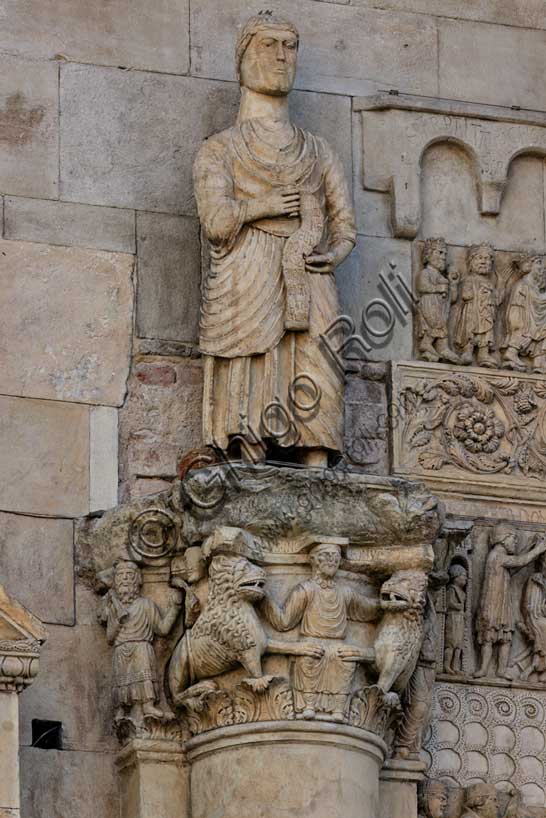 Fidenza, duomo (Cattedrale di San Donnino), sculture tra il portale maggiore e quello di sinistra: il capitello con “Daniele nella fossa dei leoni”, sormontato dalla statua con “San Simone Apostolo che mostra la via di Roma ai pellegrini”; 