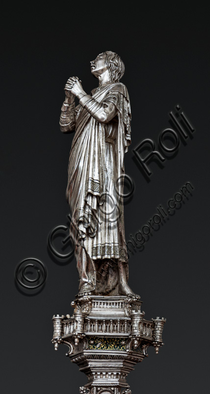 Firenze, Museo dell'Opera del Duomo (Santa Maria del Fiore): “La croce del tesoro di S. Giovanni: il verso”. Particolare di “statua di angelo orante”.La Croce è uno splendido esempio di oreficeria rinascimentale, scolpita in lamina d’argento, cesellata e smaltata da Betto di Francesco Betti, Antonio del Pollaiolo e Miliano di Domenico Dei tra il 1457 e il 1459 circa. Venne commissionata a completamento dell’altare d’argento. La Croce-ostensorio è composta da tre parti principali distinte: il Crocifisso, il fusto e la base. 