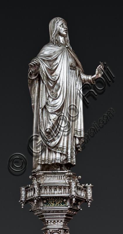 Firenze, Museo dell'Opera del Duomo (Santa Maria del Fiore): “La croce del tesoro di S. Giovanni: il verso”. Particolare di “statua della Madonna”.La Croce è uno splendido esempio di oreficeria rinascimentale, scolpita in lamina d’argento, cesellata e smaltata da Betto di Francesco Betti, Antonio del Pollaiolo e Miliano di Domenico Dei tra il 1457 e il 1459 circa. Venne commissionata a completamento dell’altare d’argento. La Croce-ostensorio è composta da tre parti principali distinte: il Crocifisso, il fusto e la base. 