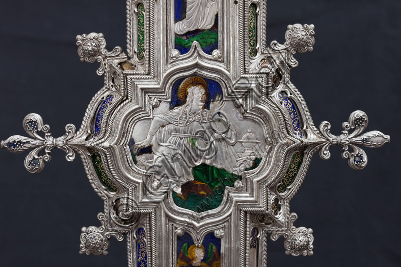 Firenze, Museo dell'Opera del Duomo (Santa Maria del Fiore): “La croce del tesoro di S. Giovanni: il recto”.Particolare della parte superiore con figura di santa o Madonna.La Croce è uno splendido esempio di oreficeria rinascimentale, scolpita in lamina d’argento, cesellata e smaltata da Betto di Francesco Betti, Antonio del Pollaiolo e Miliano di Domenico Dei tra il 1457 e il 1459 circa. Venne commissionata a completamento dell’altare d’argento. La Croce-ostensorio è composta da tre parti principali distinte: il Crocifisso, il fusto e la base. 