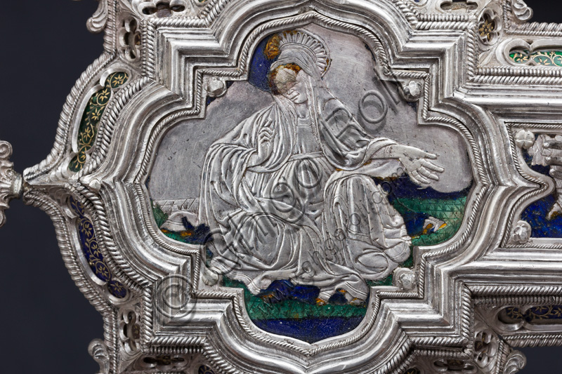 Firenze, Museo dell'Opera del Duomo (Santa Maria del Fiore): “La croce del tesoro di S. Giovanni: il recto”.Particolare della parte superiore con figura di santa o Madonna.La Croce è uno splendido esempio di oreficeria rinascimentale, scolpita in lamina d’argento, cesellata e smaltata da Betto di Francesco Betti, Antonio del Pollaiolo e Miliano di Domenico Dei tra il 1457 e il 1459 circa. Venne commissionata a completamento dell’altare d’argento. La Croce-ostensorio è composta da tre parti principali distinte: il Crocifisso, il fusto e la base. 