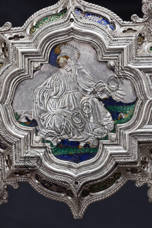 Florence, Museum of the Opera del Duomo (Museum of Florence Cathedral of Santa Maria del Fiore): “The Cross of the Treasure of St. John: the recto.”Detail of the upper part with the figure of a saint or Madonna.The Cross is a splendid example of Renaissance jewelery, sculpted in silver foil, chiseled and enameled by Betto di Francesco Betti, Antonio del Pollaiolo and Miliano di Domenico Dei between 1457 and 1459 approximately. It was commissioned to complete the silver altar. The Cross-monstrance is made up of three distinct main parts: the Crucifix, the stem and the base. 