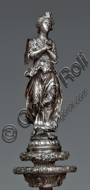 Firenze, Museo dell'Opera del Duomo (Santa Maria del Fiore): “La croce del tesoro di S. Giovanni: il verso”. Particolare di “statua di angelo orante”.La Croce è uno splendido esempio di oreficeria rinascimentale, scolpita in lamina d’argento, cesellata e smaltata da Betto di Francesco Betti, Antonio del Pollaiolo e Miliano di Domenico Dei tra il 1457 e il 1459 circa. Venne commissionata a completamento dell’altare d’argento. La Croce-ostensorio è composta da tre parti principali distinte: il Crocifisso, il fusto e la base. 