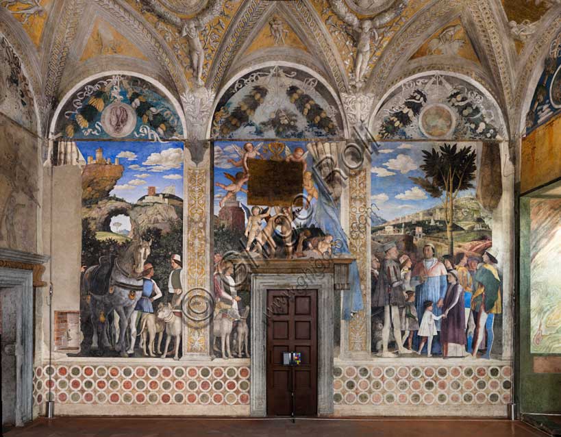 Ducal Palace: south-west wall of the “Bridal Chamber or Camera Picta", which is a room located in the north-east tower of the Castle of San Giorgio in Mantua. It is famous for the cycle of frescoes that covers its walls, a masterpiece by Andrea Mantegna, created between 1465 and 1474.The wall, on the theme of “The Meeting” is divided into three sectors. In the one on the left the actual meeting takes place, in the central one some cherubs hold a dedicatory plaque and in the one on the right the marquis's court parades.The Marquis Ludovico is represented in the Meeting, this time in official guise, perhaps flanked by Ugolotto Gonzaga, son of his deceased brother Carlo. His son Francesco who is a Cardinal is in front of him. Below them are the sons of Federico I Gonzaga, Francesco and Sigismondo, while their father Federico is on the far right: the generous folds of his dress are a ploy to hide his kyphosis. Federico is in conversation with two characters, one in front and the other in the background, indicated by some as Christian I of Denmarkand Frederick III of Habsburg, figures who well represent the family's pride in royal kinship. Finally, the boy in the center is the last son of the marquis, the prothonotary Ludovico. In the background an ideal view of Rome is represented, in which there ancient monuments such as the Colosseum, Castel Sant'Angelo, the pyramid of Cestius, the theater of Marcellus, the Nomentano bridge, the Aurelian Walls, etc. cani be recognised. Mantegna also invented some monuments  such as a colossal statue of Hercules. On the right there is also a cave where some quarrymen are at work sculpting blocks and columns.